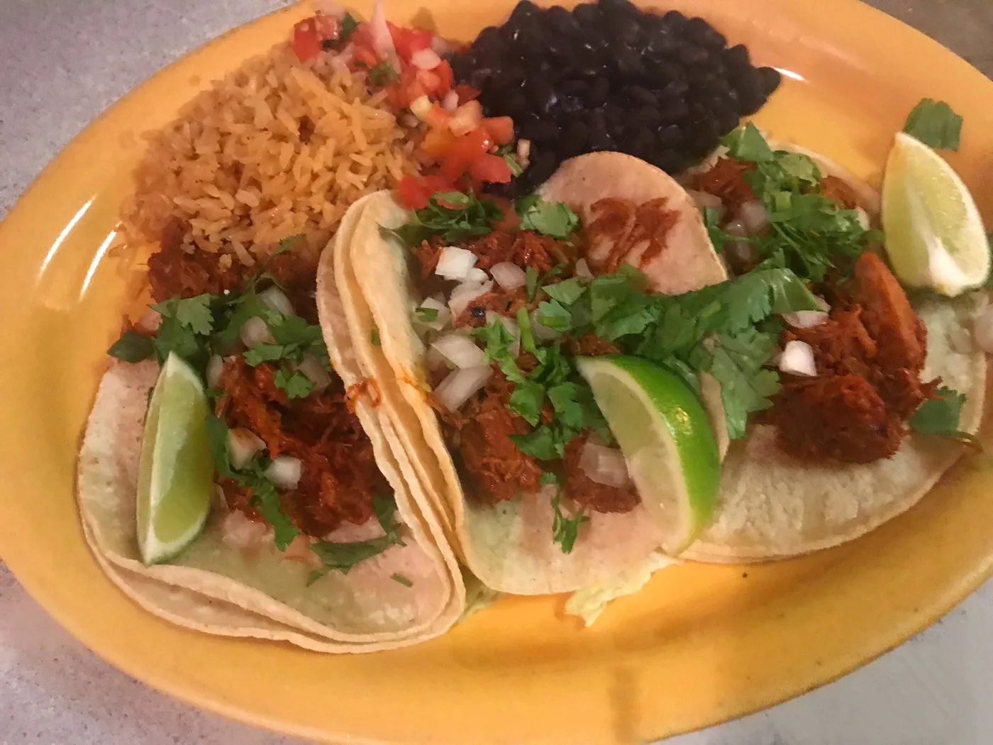 Three tacos with cilantro, onion and lime alongside Mexican rice and black beans